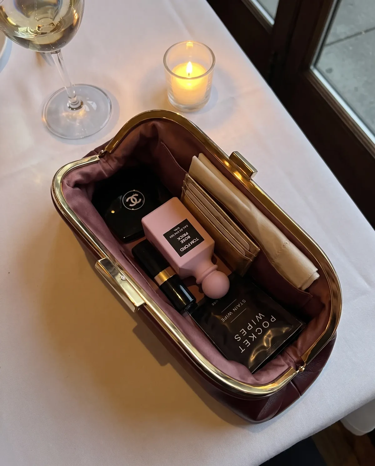 Open burgundy clutch containing a Pocket Wipes stain wipe sachet, cosmetics and a card holder